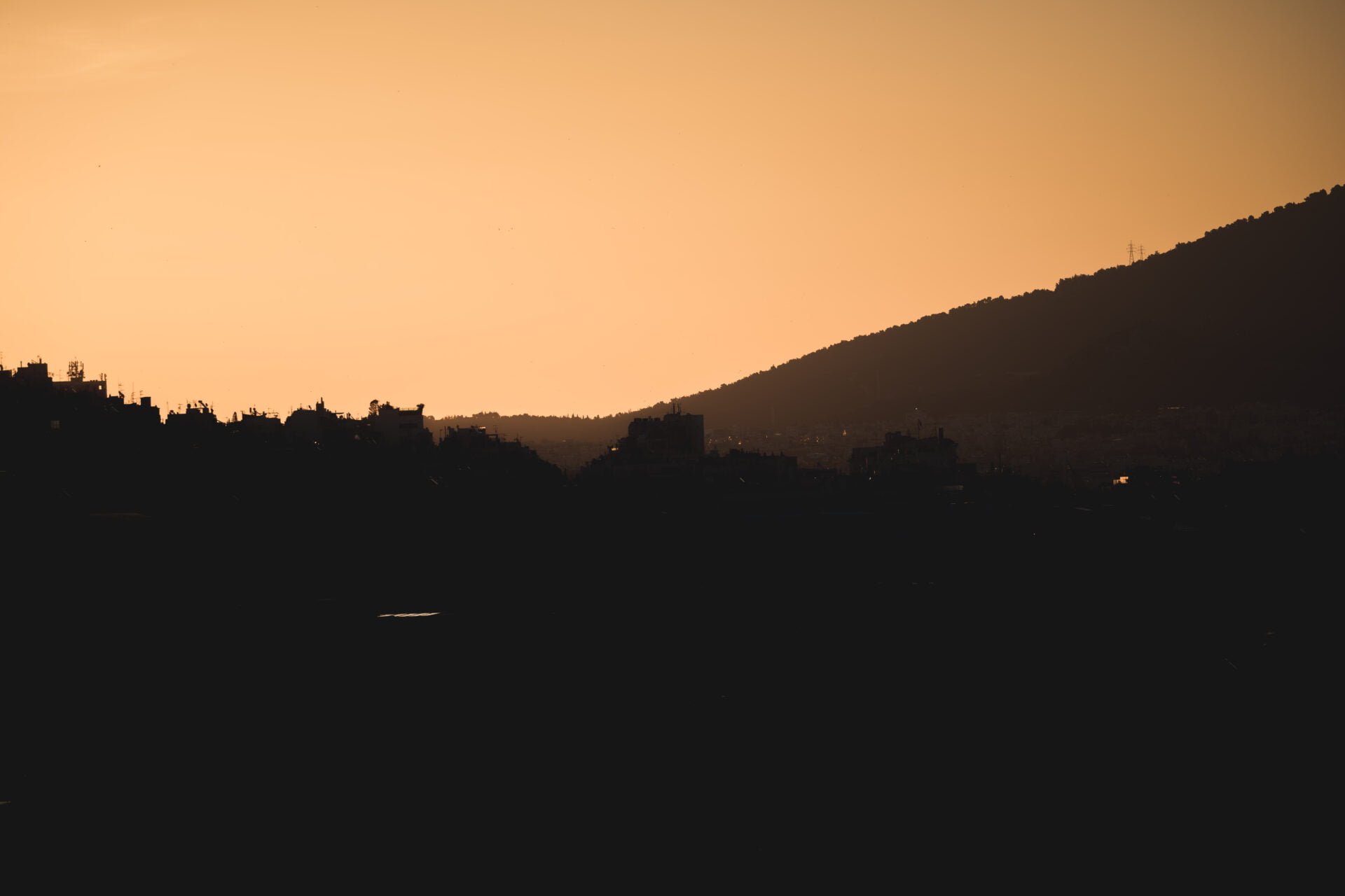 Sunrise Silhouettes - Milan Ivanovic Photography The silhouette of a cityscape against an amber sky at dusk, with outlines of buildings and a hillside faintly visible, evoking the peaceful transition from day to night.